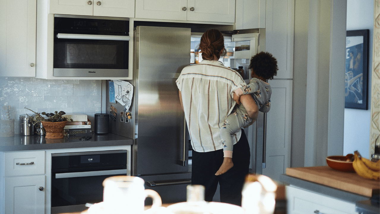 a person holding a child as they look into the refrigerator