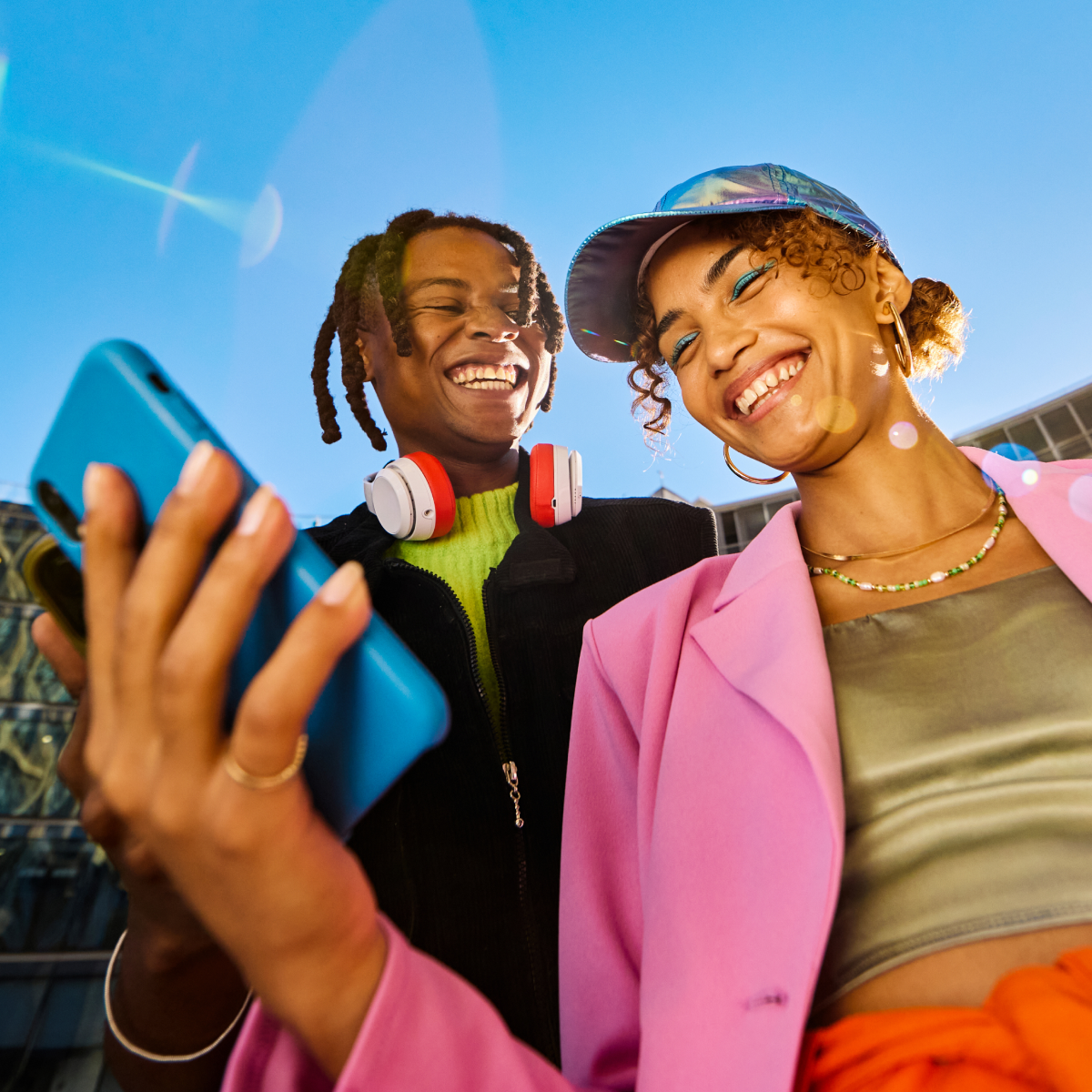 two people smiling while looking at a mobile phone
